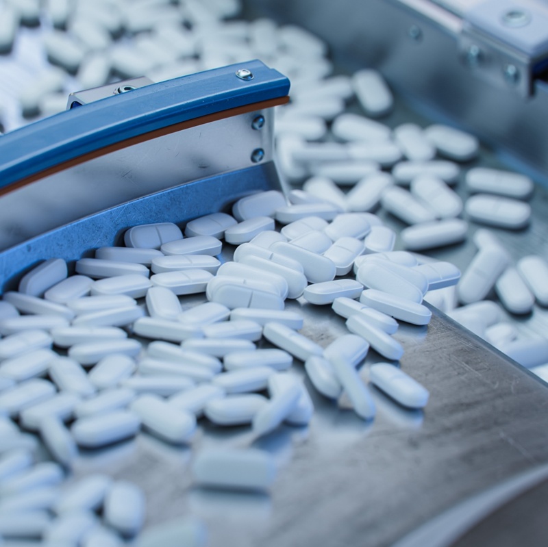 Tablets and Capsules Manufacturing Process. Close-up Shot of Medical Drug Production Line. White Painkiller Pills are Moving on Conveyor at Modern Pharmaceutical Factory.